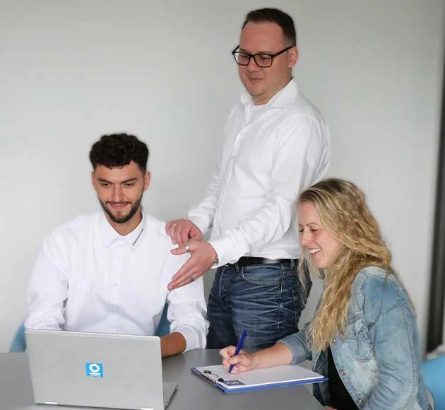 Three employees are discussing something together on a laptop in the office