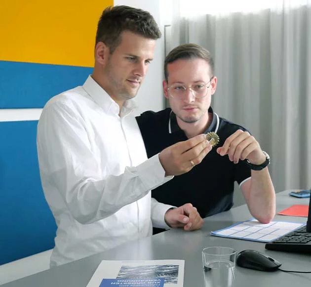 Two employees are examining a gear together in the conference room