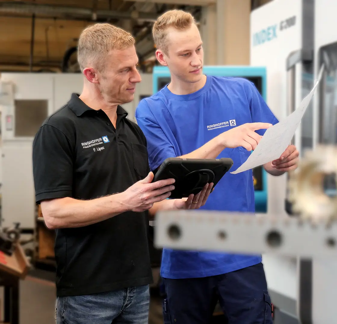Franjo Lipec is discussing a technical drawing with an apprentice at the CNC machine